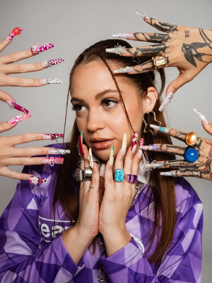 Clara em retrato editorial com as mãos junto ao rosto, cercada por unhas decoradas