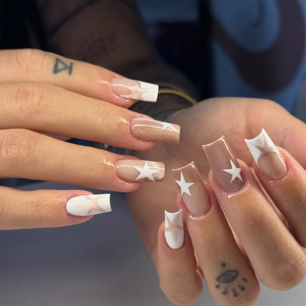 Unhas com estrelas brancas sobre base nude com brilho
